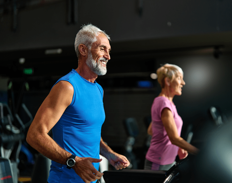 Man & woman jogging on treadmills to improve fitness & overall health.